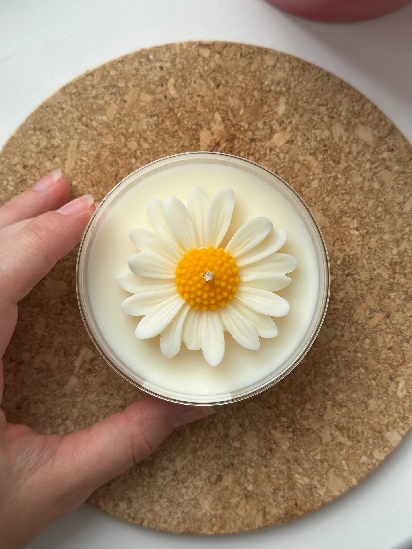 Hand holding a candle with a daisy design on a cork coaster