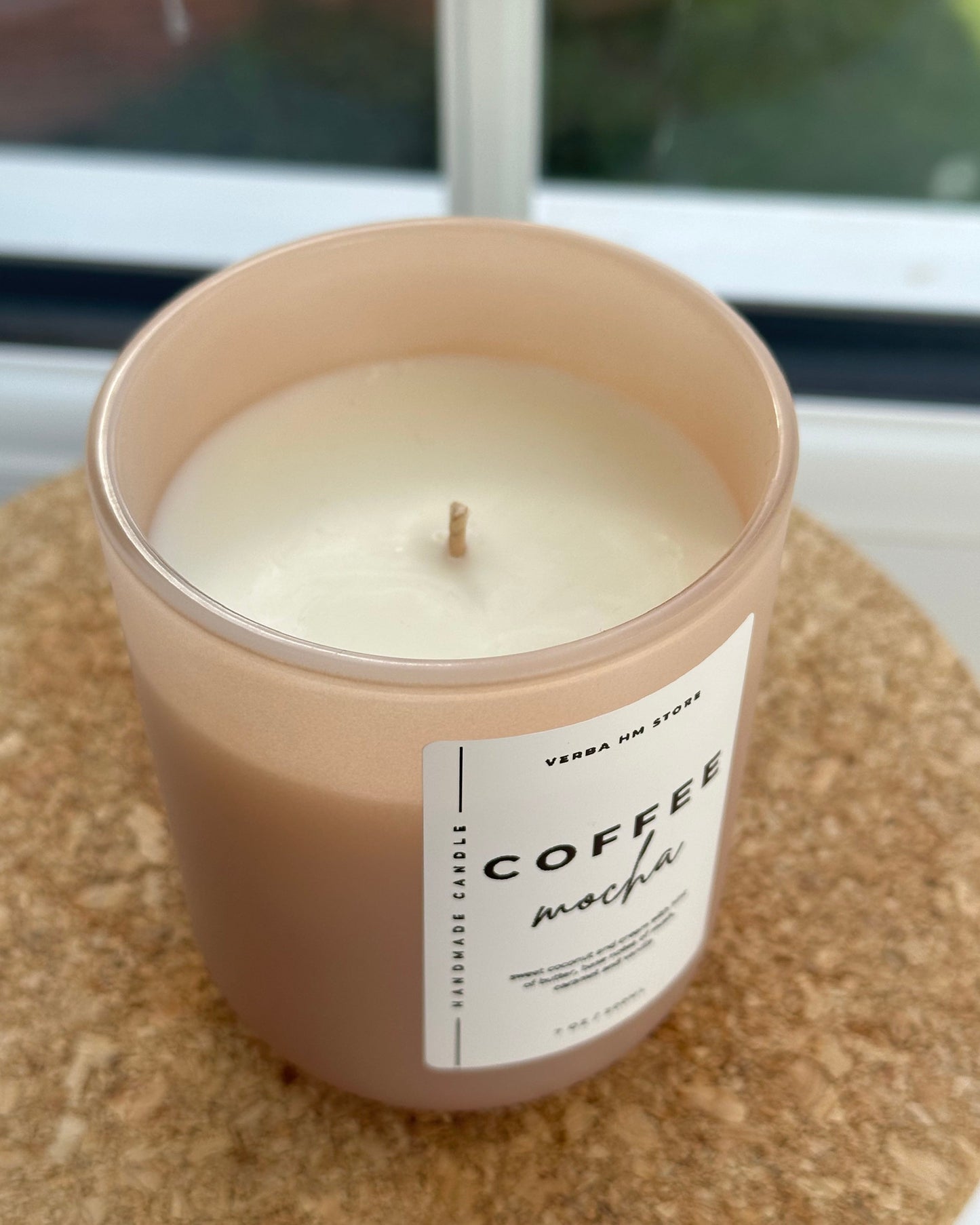 Candle in a beige container labeled 'Coffee Mocha' on a cork surface.