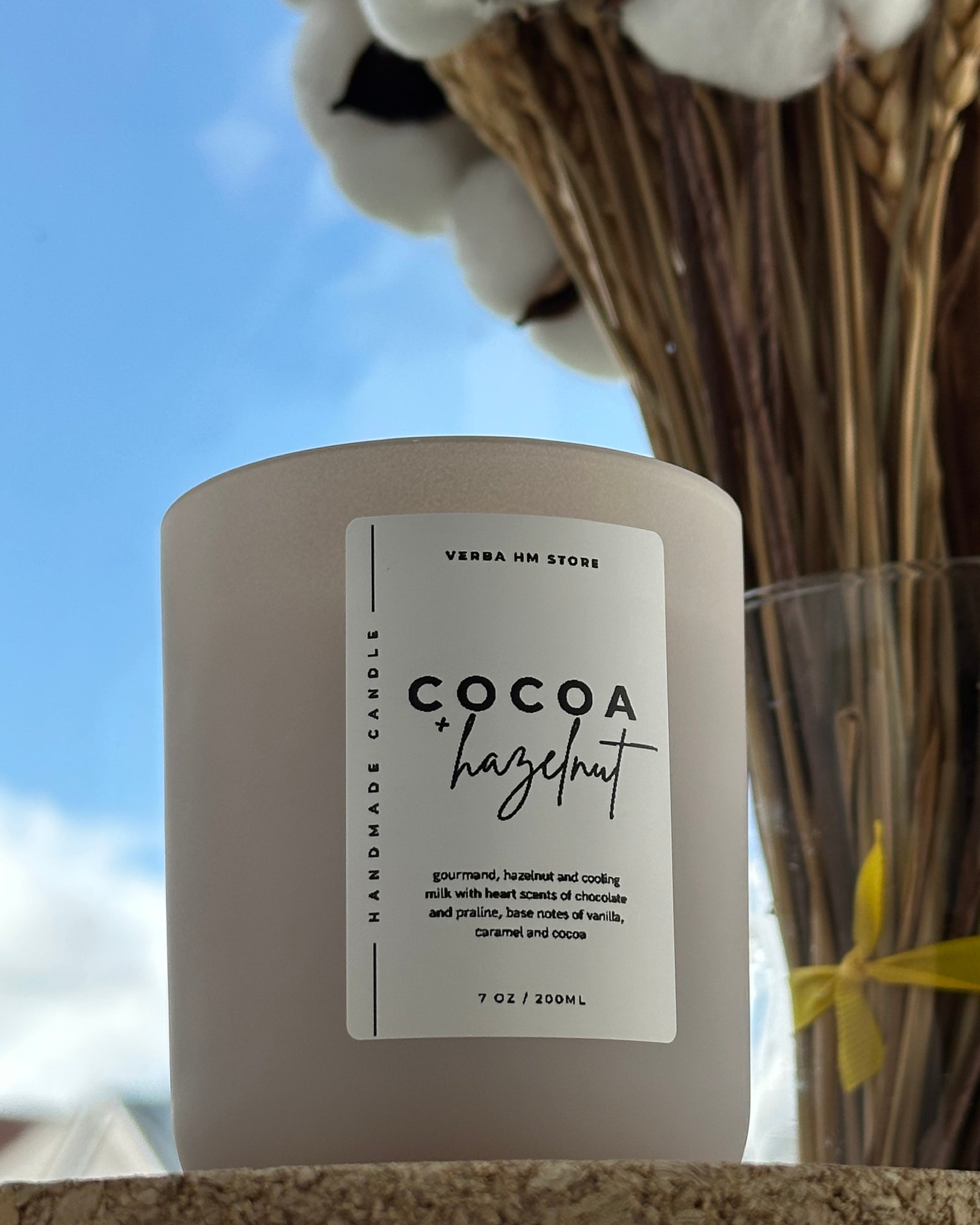 Candle labeled 'Cocoa Hazelnut' with a blurred background of cotton and flowers.